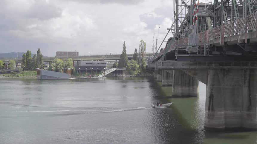 A motorboat travels along a river and under a bridge on a cloudy day