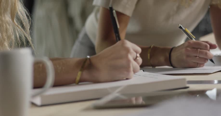 Women are writing in notebooks on a desk