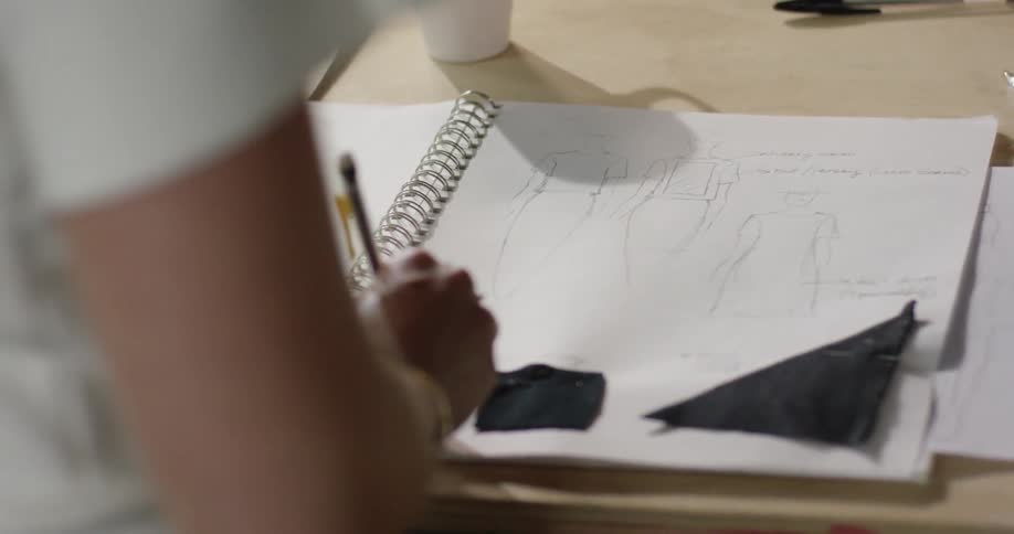 A person is drawing in a notebooks with a mug next to the book