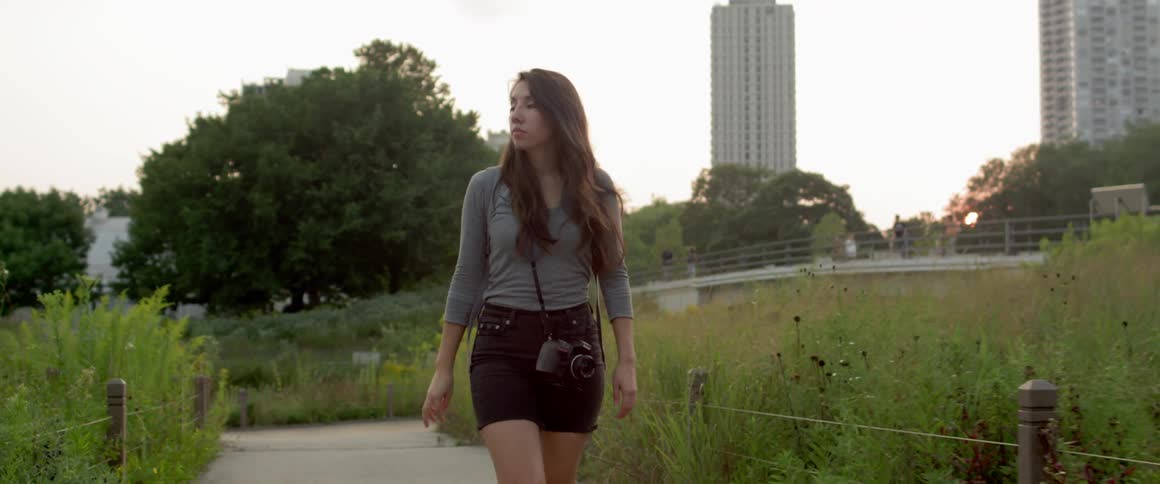 A young woman walks a city trail carrying a camera