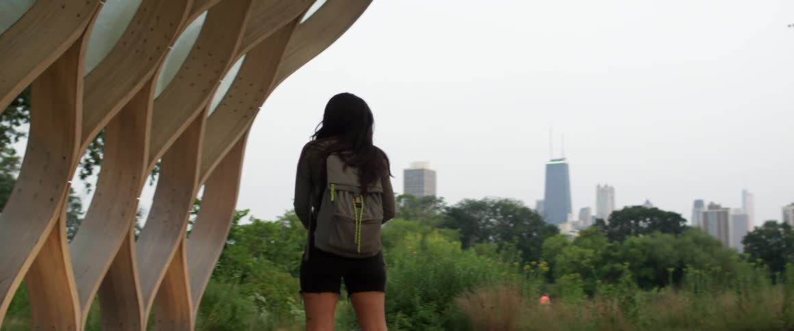Young woman wearing a backpack studying a structure on the outskirts of a large city