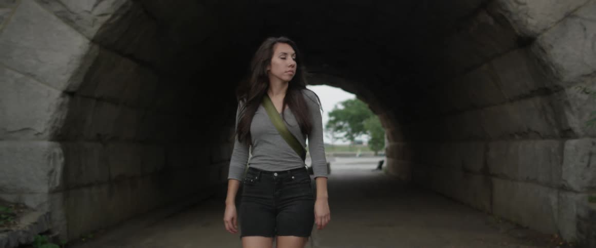 A woman walks through a dark tunnel on a cloudy day