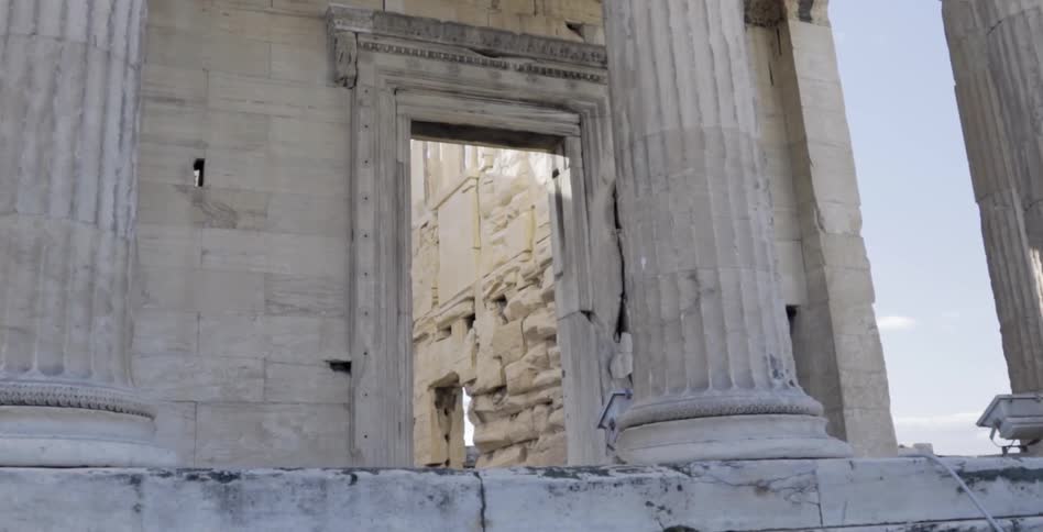 A large stone building has stone pillars before a doorway