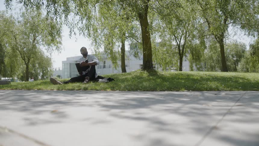 Man sits under a tree reading a book then looks up to the sky