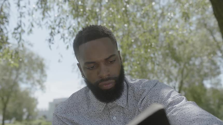 A man makes notes in a book under a tree outside on a breezy day