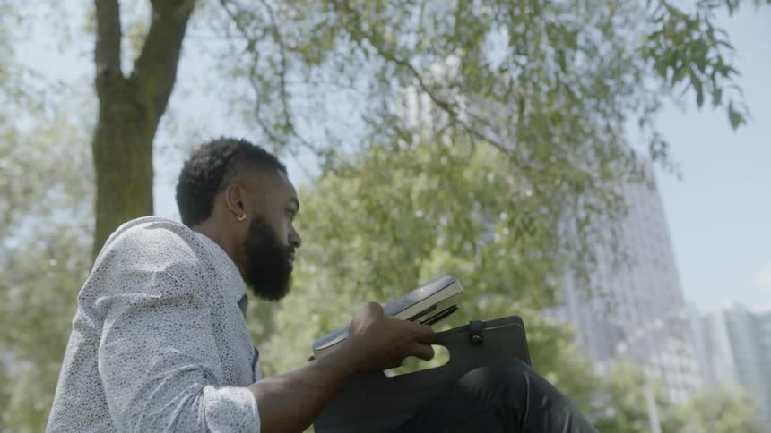 Man wearing earrings and holding notebook gets up and takes off on a sunny day