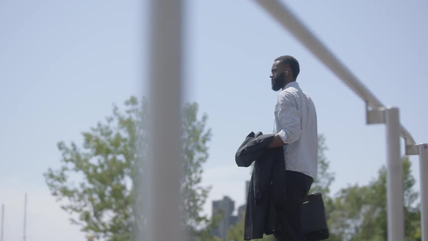Black man leaving the office walking to parking lot holding his briefcase and coat