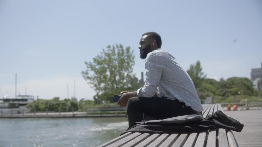 Black man sitting on bench next to a lake relaxing