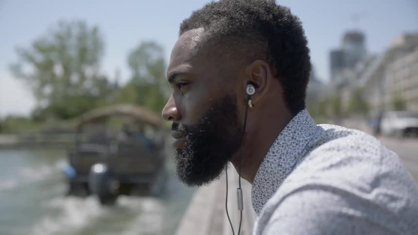 Man sits on the side of a lake and listens to music through is earbuds