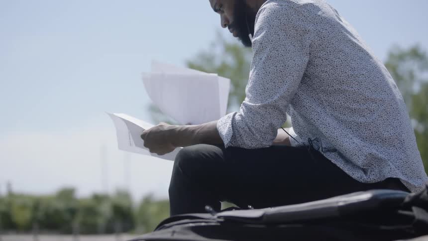 Man who has earrings and listening to music with headphones sits down and check papers during the day