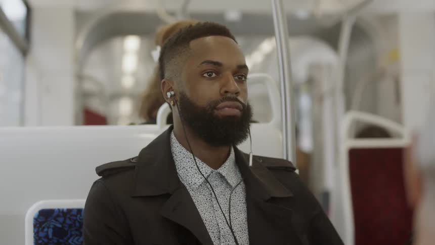Black man traveling on the metro wearing a coat and earphones