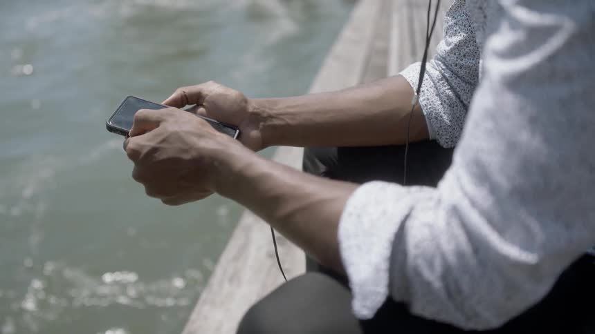 A man is holding a cell phone by water