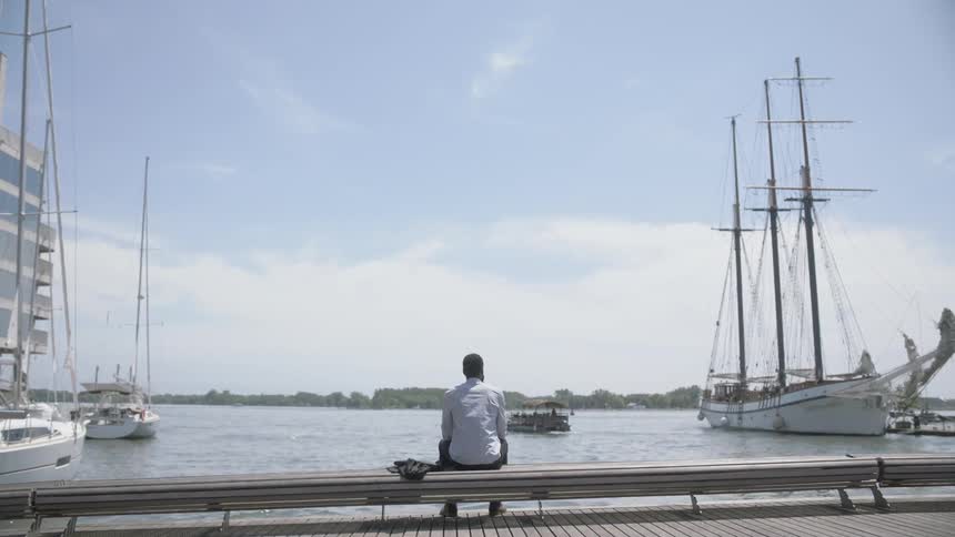 Man sits on dock watching ships in harbor