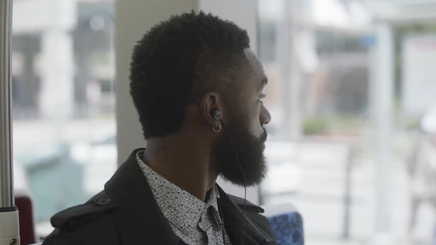 A young black man sits on a bus with earbuds in