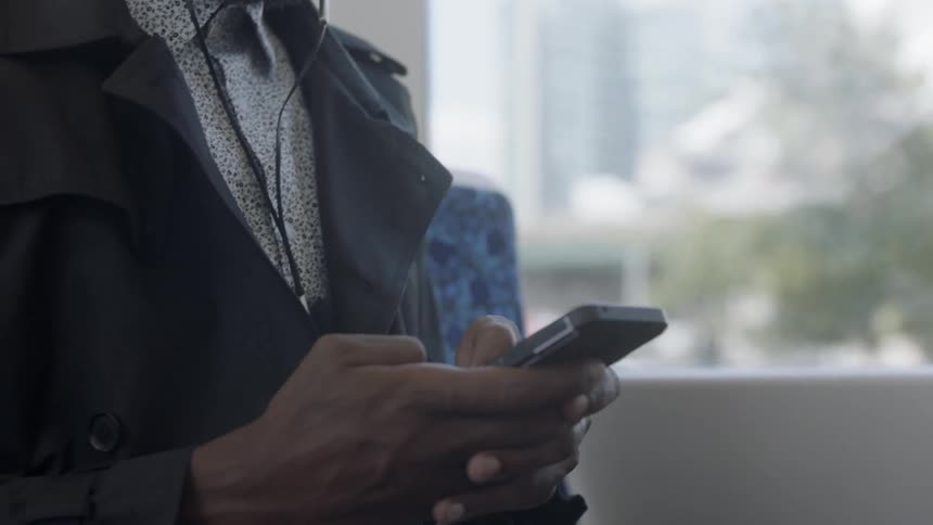 A man wears headphones and uses his phone as he rides public transportation