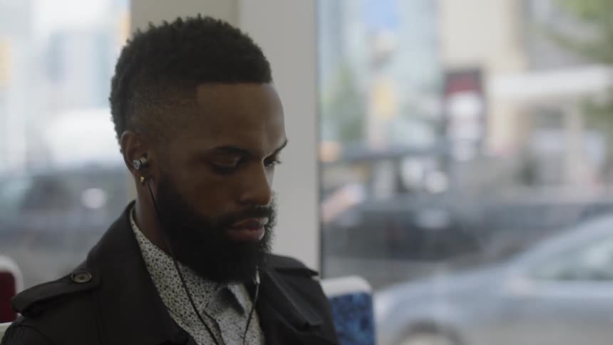 A black commuter rides the bus while listening to music during the day