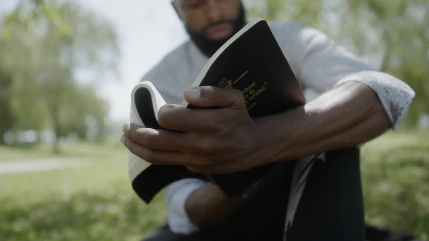 A black male sitting on the grass reading a book