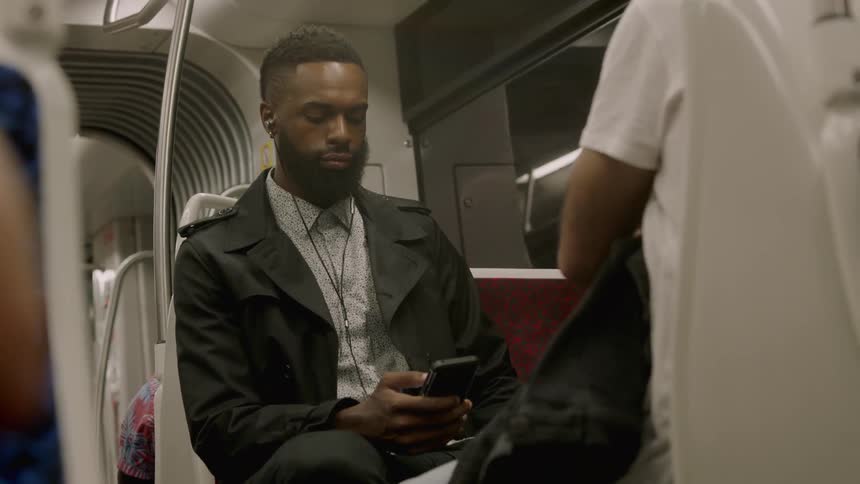 Man who listens to music and looks at his phone sits on a subway