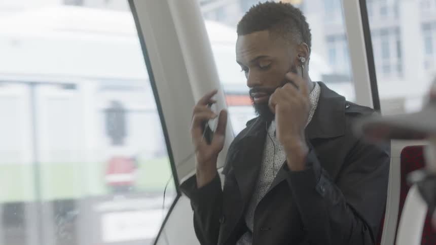 A man rides on a bus and puts earbuds in his ears