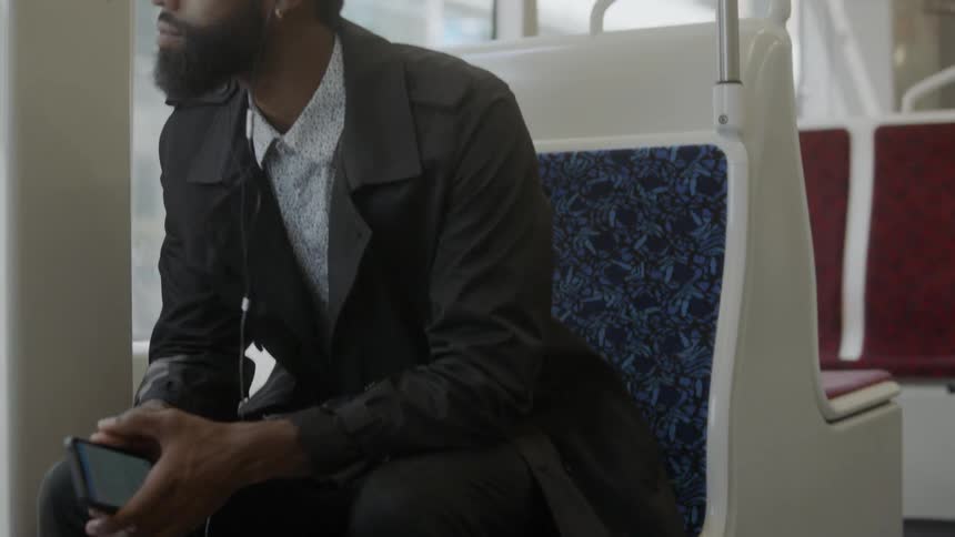 A black male with ear buds in his ears sitting on a bus