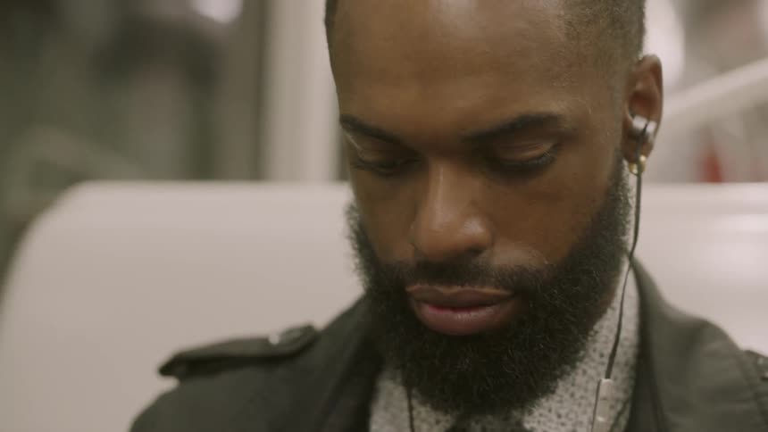 Young bearded man listens to headphones on public transportation