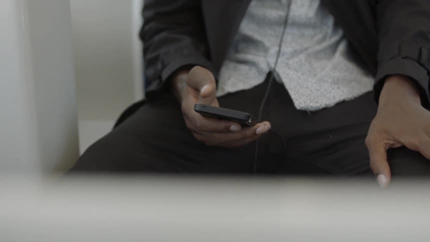 A man in dark clothing sits and holds a smart phone in his hand