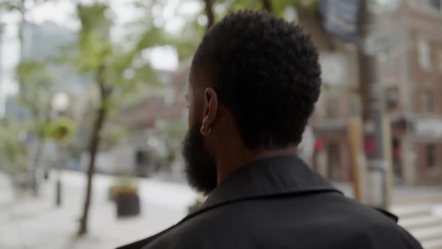A black man walks on a sidewalk in a city