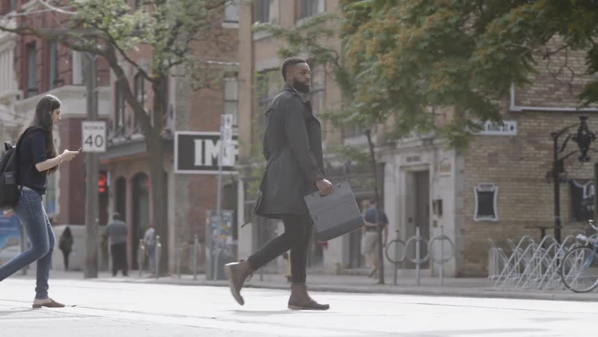 A man with a briefcase and black jacket crosses a city street
