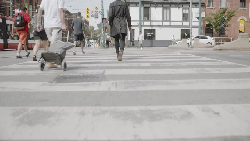 A man in brown boots and a green jacket walks down a city street in the daytime
