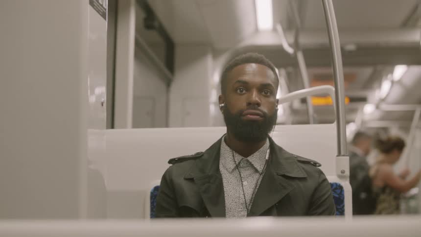 A black man has earbuds in while sitting in a seat on the subway