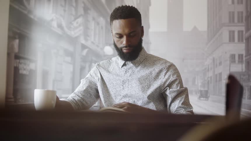 A black person sitting down at a table reading book
