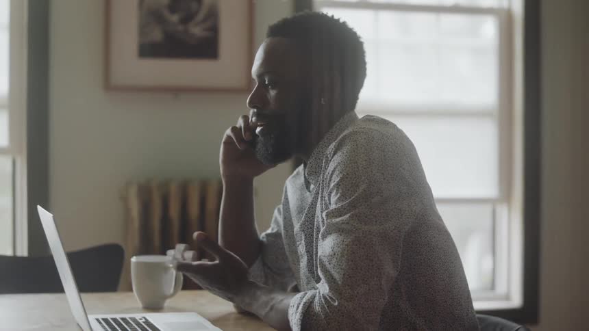 Man talks on phone while sitting in front of his laptop at a desk