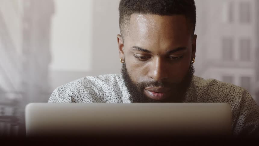 Black man working on his laptop while drinking a cup of coffee