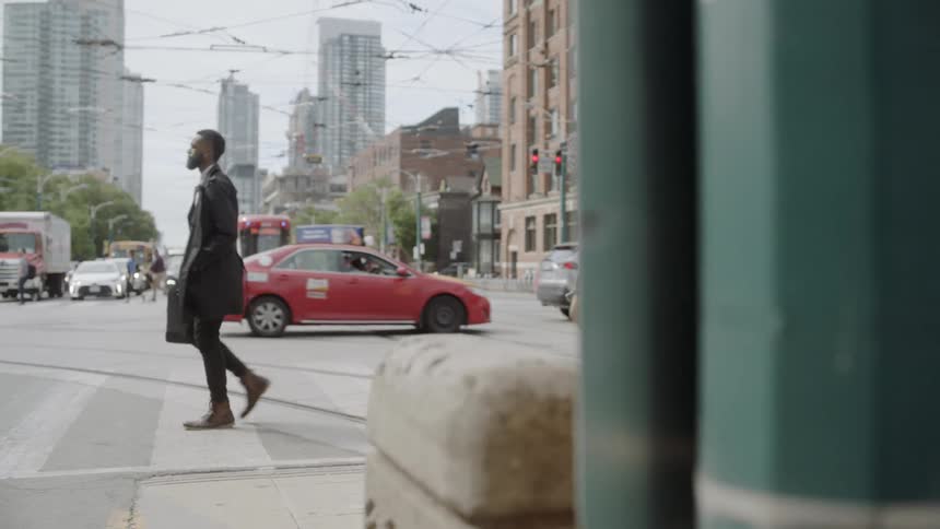 A young black man crosses the street while carrying a briefcase
