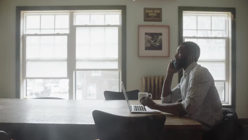 A man talking on the phone and working on a laptop at a table