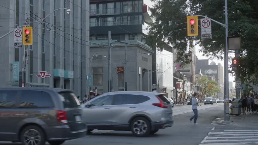 Cars drive through an intersection in a downtown area while people cross the street