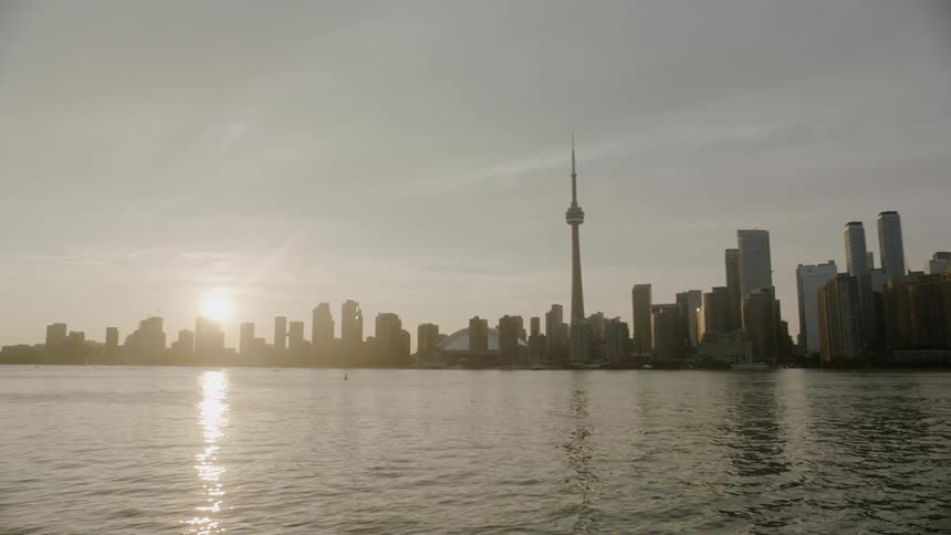 The sun is setting very low over a waterfront metropolitan city that is full of numerous skyscrapers
