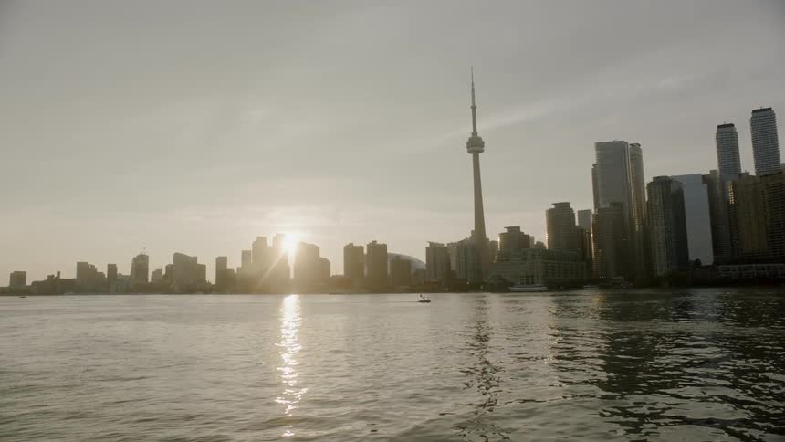 Water rippling calmly as the sun sets behind the buildings in the city