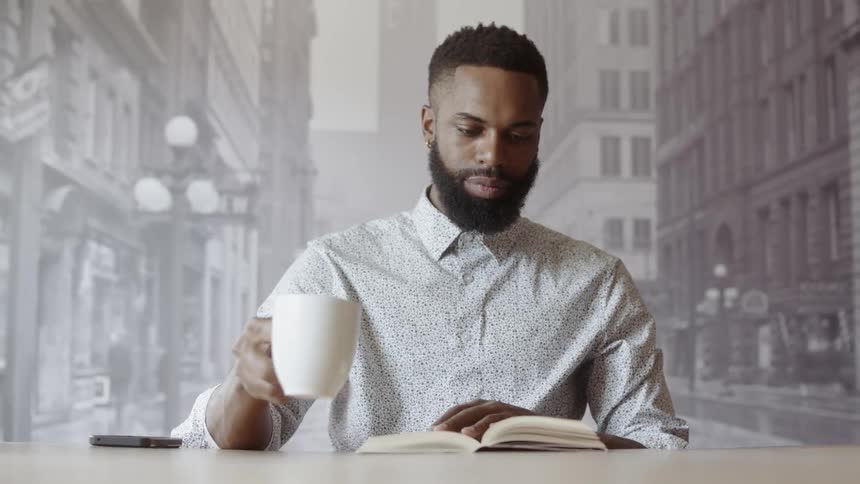 Man reading a book and drinking a hot beverage