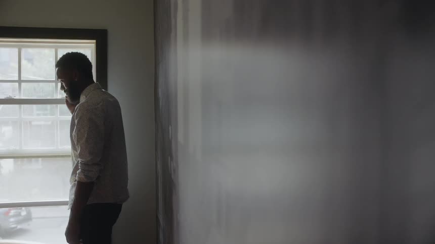 Man standing inside building near window talks on cell phone