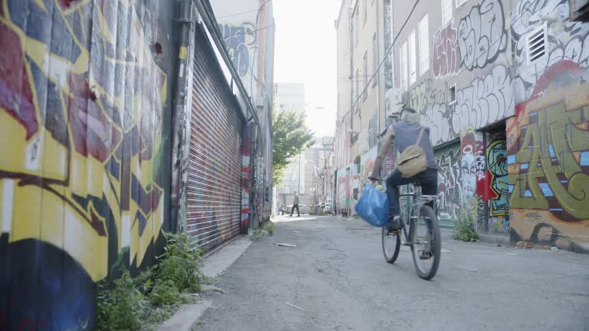 A person rides a bike down an alley filled with graffiti