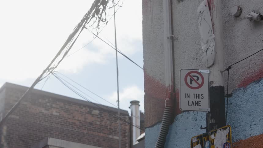 Signs pipes and wires hang off of a building on a city street