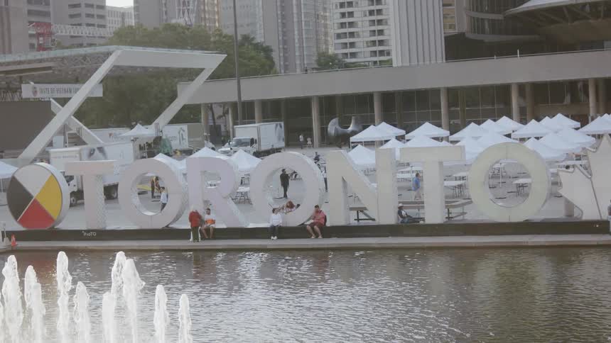 Numerous people sit and walk around a large landmark sign by a fountain