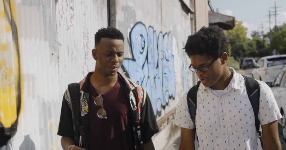 Two young black men walking together near a graffiti wall
