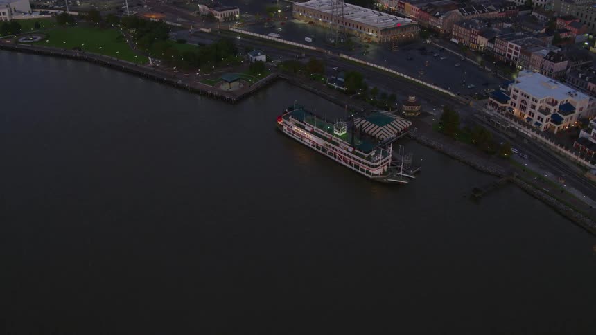 A large steam powered paddle boat is docked at the pier at the edge of a large downtown area of a city