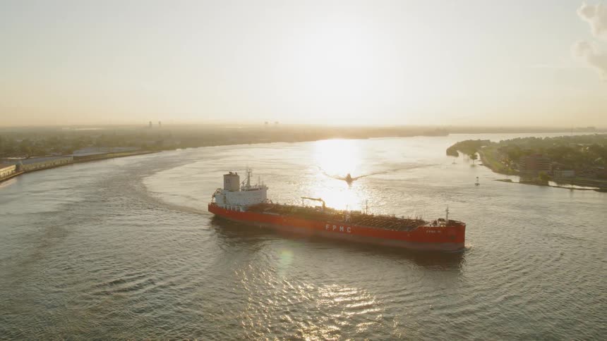 A container ship with a crane on its deck sails along a river during a sunset