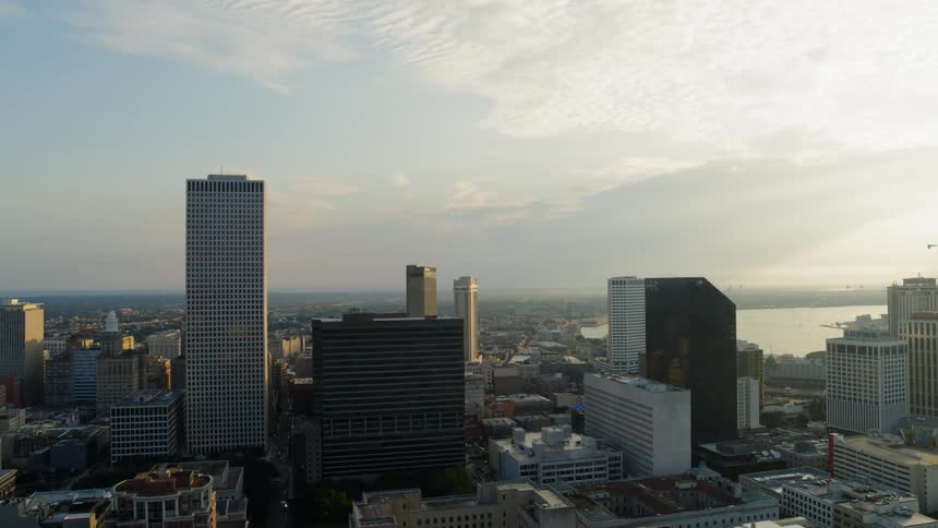 A city landscape set by a body of water is viewed from the air at low sun