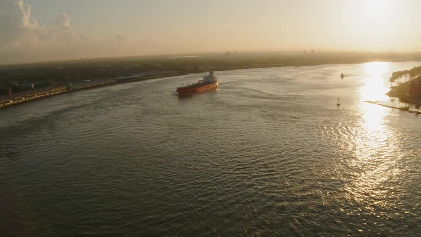 A barge travels through the water near shore at sunset