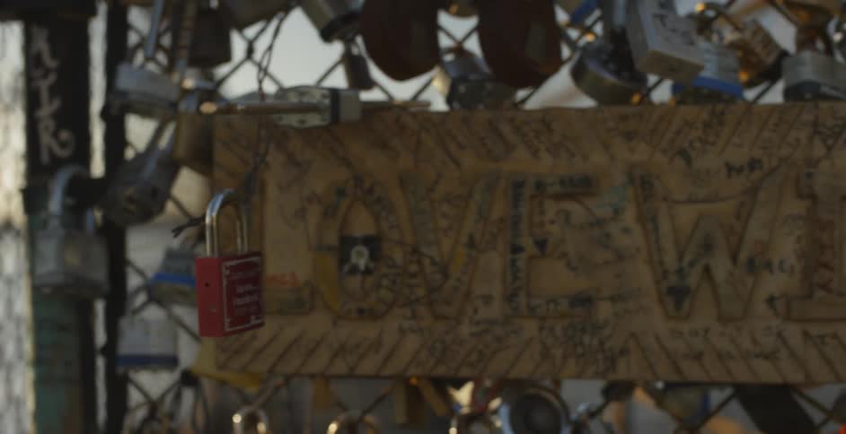 The camera pans across love locks hooked to a fence next to water