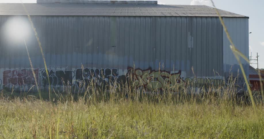 A man with a backpack walks by a metal building covered in graffiti